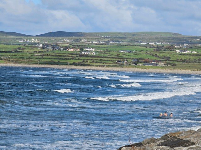 waves breaking on the rocks along the beach with a few dippers in the water
